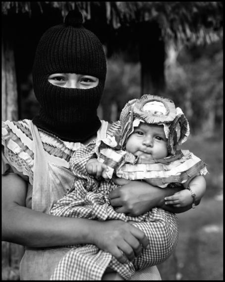 Mustavalkoisessa kuvassa kommandopipoinen nainen pitää sylissään hienosti puettua vauvaa. 