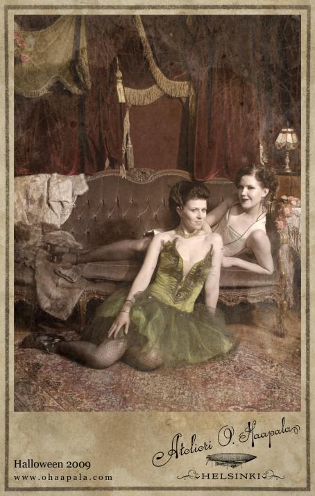 Kaksi naista, joista toinen makoilee sohvalla ja toinen istuu sohvan edessä. Edessä olevalla on päällään vihreä mekko. Taustalla näkyy raskaat punaiset verhot. Alareunassa on teksti:"Halloween 2009, Atelieri O.Haapala, Helsinki".
