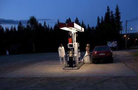 Pimeässä maisemassa valaistu bensa-asema, jossa häämekkoon pukeutunut nainen tankkaa punaista autoa. Hän katsoo vähän kauempana seisovaa ihmistä, jolla on valkoiset housut ja valkoinen pitkä paita.