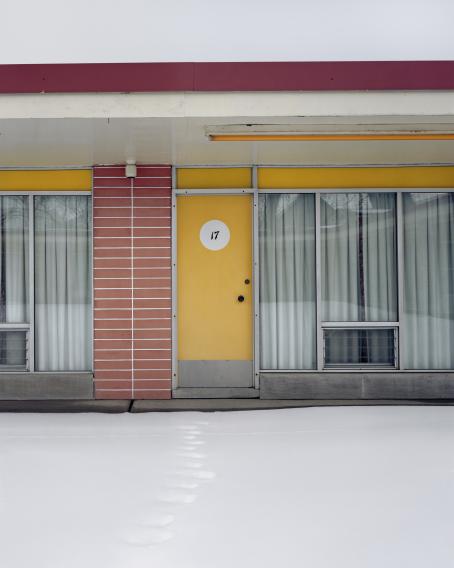 Rakennuksen seinusta. Korkeiden ikkunoiden eteen on vedetty haaleanvihreät pitkät verhot. Ovi on keltainen ja siinä on numero 17. Lumessa näkyvät yhdet jalanjäljet ovelle. 