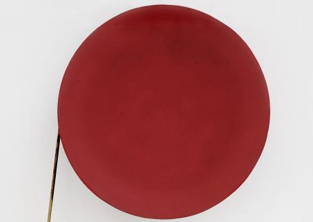 Vaaleaa taustaa vasten iso punainen ympyrä, jonka vasemmalta puolelta lähtee alaspäin suora keppi tai tikku.