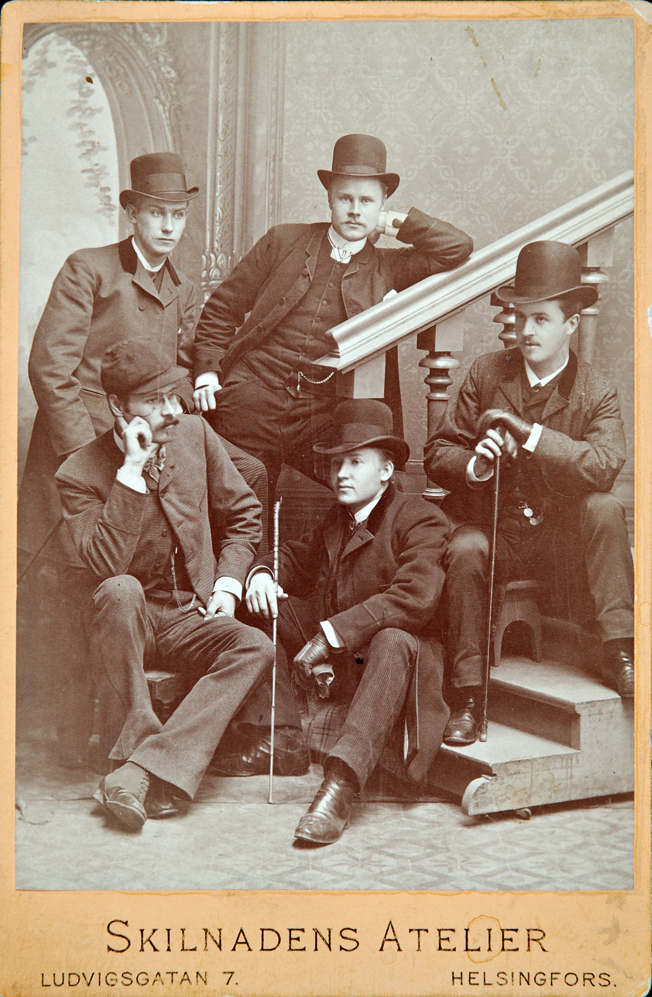 Kaveriporukka koolla. Renessanssityyliseen palatsiin on ilmestynyt puiset, pyörillä liikuteltavat portaat. Kuva: Skilnadens Atelier, 1885, kabinettikortti. D2015:81/93