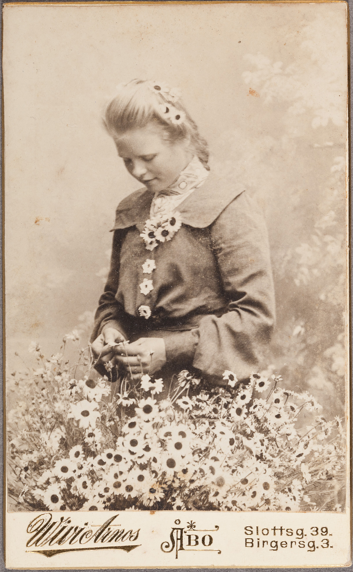 Kukkaistyttö kedolla. Kuva: Wivi Arnos Fotografiatelier, 1900, visiittikortti. Suomen valokuvataiteen museo. D1999:65/29