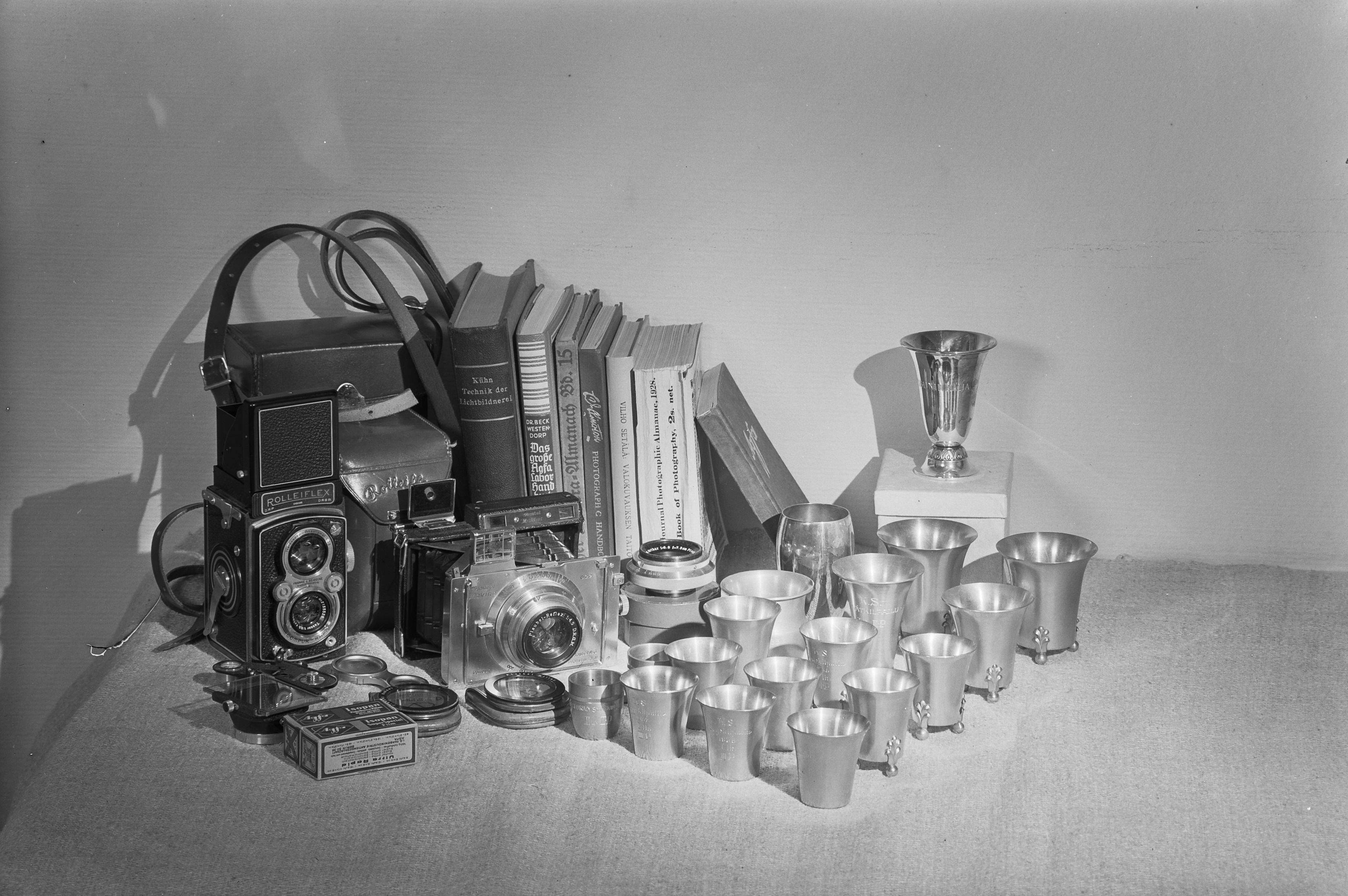 Asetelmassa kameroita, valokuvauskirjallisuutta, objektiiveja ja palkintoja. Aarne Pietisen Rolleiflex ja Plaubel Makina . 1944. Suomen valokuvataiteen museo