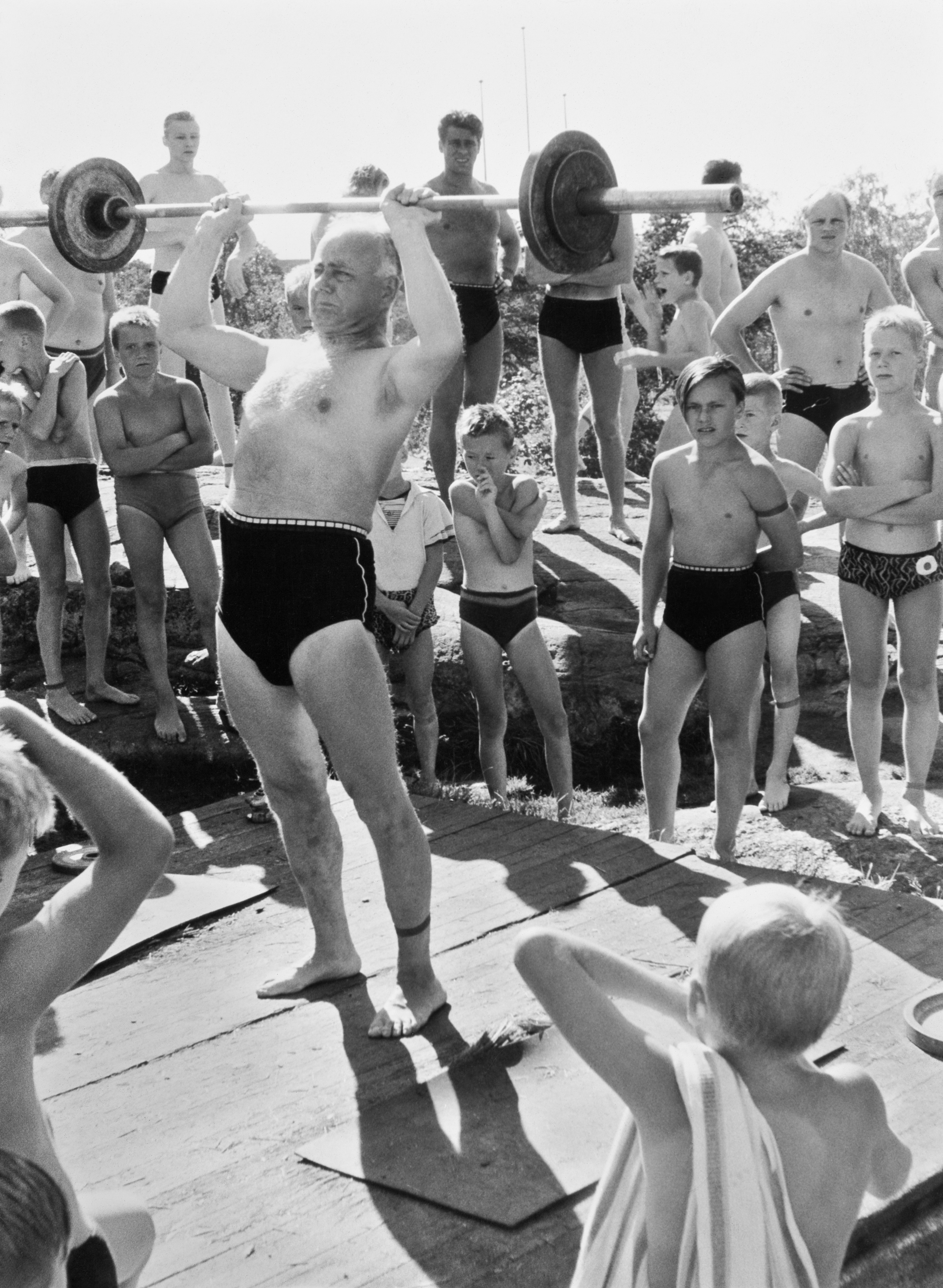 Kesälomalla saa myös kuntoilla! Tässä voimannostoa uimastadionilla 50-luvun loppupuolelta, jolloin K.G. Roos dokumentoi elämää Helsingissä. Kuva on julkaistu myös Jörn Donnerin teoksessa "Ihmisten Helsinki" (1961, WSOY). Suomen valokuvataiteen museo.