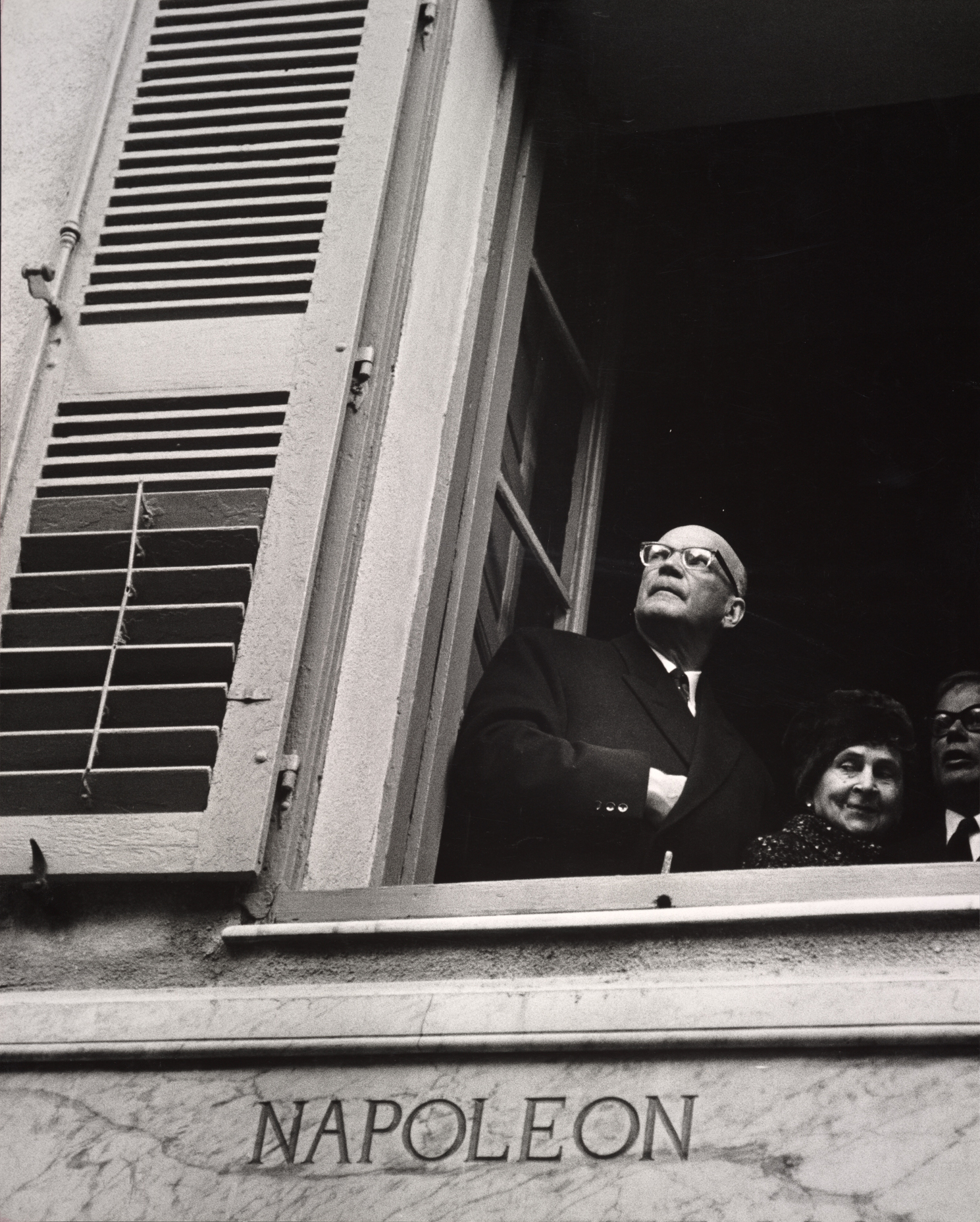 Mustavalkoisessa kuvassa alaviistosta kuvattu presidentti Urho Kekkonen seisoo avoimella ikkunalla. Hänellä on toinen käsi rinnalla puvuntakin sisällä, ja hän katsoo yläviistoon. Hänen takanaan on kaksi muuta ihmistä, mies ja nainen. Ikkunan alla seinässä lukee Napoleon. 