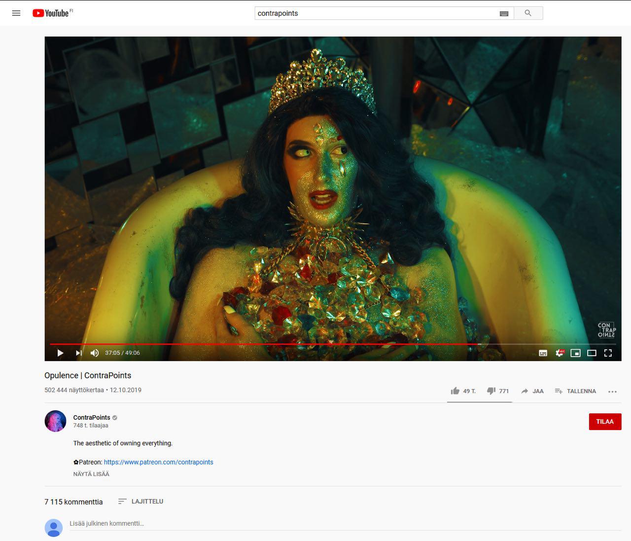 Kuvakaappaus Youtube-videosta. Kuvassa henkilö makaa kylpyammeessa. Toinen puoli hänen kasvoistaan on kultaisena kiiltävän meikin peitossa, hänellä on kultainen kruunu päässään ja rinnallaan kiiltäviä jalokiviä tms.