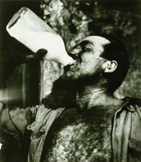 Mustavalkoisessa kuvassa mies juo maitoa lasipullosta. 