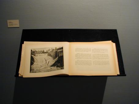 Näyttelyssä esillä oleva kirja, jossa näkyy Inhan valokuva koskesta sekä tekstiä, josta ei saa selvää.