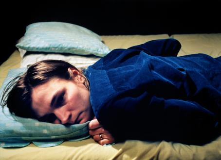 Henkilö sinisessä paidassa makaa mahallaan sängyllä. Hänen vieressään on tyhjä paikka.