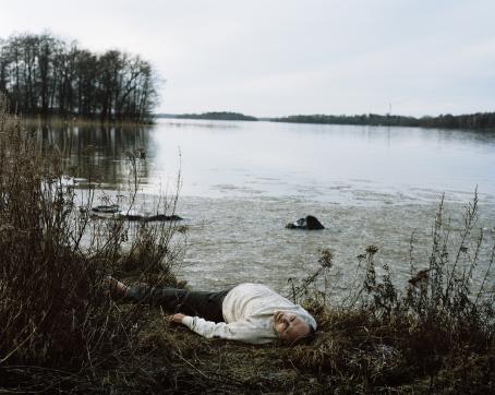 Henkilö makaa selällään järven rannalla rantakasvillisuuden keskellä.