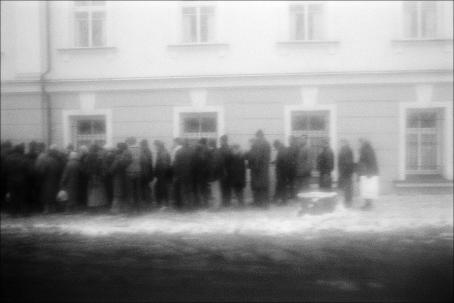 Rakeisessa, mustavalkoisessa kuvassa jono ihmisiä rakennuksen edessä.
