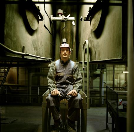 Mies istuu haalarit päällä tehdasmaisessa ympäristössä.