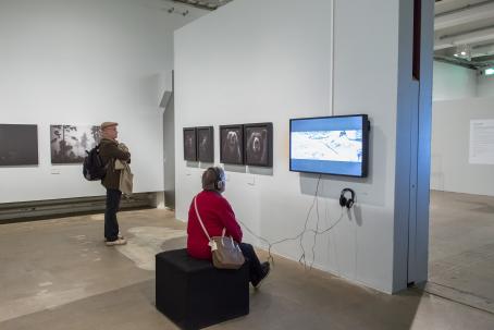 Näyttelyssä kävijä istuu katsomassa Willamon videoteosta kuulokkeet päässä.