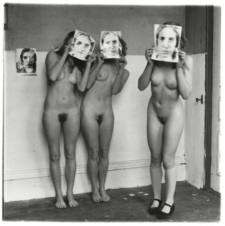 Kolme alastonta naista, jotka kaikki pitelevät kasvojensa edessä paperia, jossa on jonkun ihmisen kasvot. Myös seinällä on yksi paperi jossa on kasvot. Yhdellä naisista on mustat kengät jalassa.