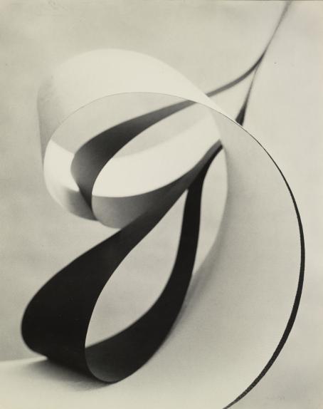 Allan Grönvall: Eteenpäin, abstraktio, 1957-58. Hopeagelatiinivedos, Suomen valokuvataiteen museo, D1985:9/1015. Valkoinen leveä nauha, joka tulee kuvan vasemmasta alanurkasta ja kiertyy silmukalle. Sen sisällä on ohuempia mustia nauhoja, jotka ovat kiertyneet silmukalle.