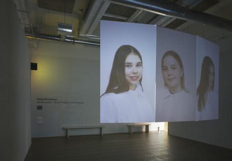 Näyttelytilassa oleva teos jossa on vierekkäin kolme muotokuvaa, joissa olevilla nuorilla on valkoiset albat päällään.