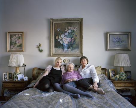 Parisängyllä makaa tyynyihin nojaten kolme eri-ikäistä naista. Vasemmanpuoleinen on nuorin, keskimmäinen on vanhin ja oikeanpuolimmainen jostain heidän väliltään. Sänky on peitetty muovilla. Takana seinällä on kolme taulua, joissa on kukkia. Sängyn molemmin puolin on yöpöydät, joissa on samanlainen lamppu. 