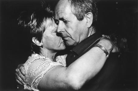 Mustavalkoisessa kuvassa mies ja nainen halaavat toisiaan. Naisen kasvot jäävät osittain miehen kasvojen taakse. Naisen käsi on miehen olalla ja miehen käsi on naisen ympärillä. 