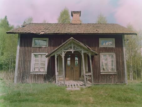 JH Engström, sarjasta From Back Home. JH Engströmin on kuvannut sarjan kotimaisemissaan Ruotsin Värmlannissa. Hieman ränsistynyt vanha puutalo. Keskellä olevan sisäänkäynnin yläpuolella oleva katos on hieman vinossa. Talon edustalla on vihreää nurmikkoa, ja takana vihreää koivikkoa.
