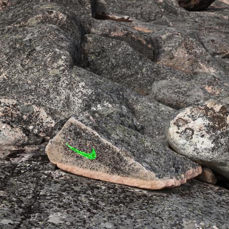 Kivikossa etäisesti kenkää muistuttava kivi, johon on piirretty vihreällä Niken logo. 