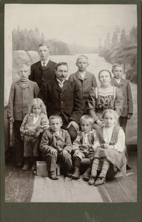 Mustavalkoisessa kuvassa mies ja nainen sekä kahdeksan lasta, luultavasti perhe. Pienimmät lapset ja vanhemmat istuvat, muut seisovat. Kaikilla on vakava ilme. Taustakuvana on kallioinen jokimaisema