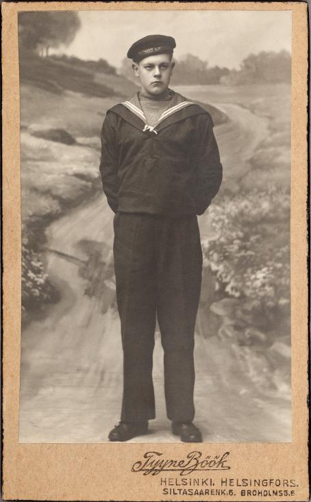 Mustavalkoisessa kuvassa seisoo nuori mies kädet selän takana. Hänellä on yllään jonkinlainen luultavasti merimiehen asu. Hänellä on vakava ilme. Taustana on kuva kapeasta tiestä, jota reunustaa niityt. 