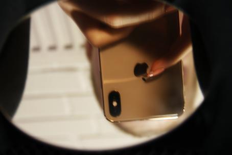 Pyöreä peili, josta heijastuu ylösalaisin iPhonea pitelevä käsi hieman epäterävänä. Puhelimen takana näkyy kasvot, jotka puhelin kuitenkin peittää suurimmaksi osaksi. Kuvan reunat ovat mustat. 