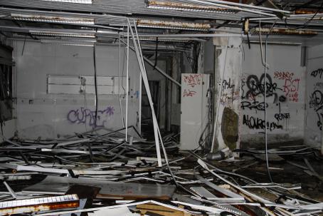 Salamalla valaistu hylätty huone, jonka lattia on täynnä roinaa ja romua, katosta roikkuu jotain rakenteita ja seinillä on graffiteja.