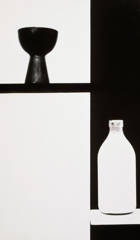 Kuvan vasen puoli on valkoinen. Ylhäällä on musta taso, jossa on musta esine. Kuvan oikea puoli on musta. Alhaalla on valkoinen taso, jossa on valkoinen pullo.
