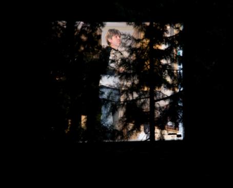 Pimeyden keskellä ja puitten takana ikkunassa mies. 