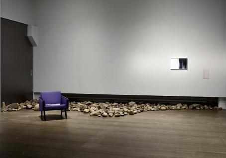 Huone, jonka seinänvierustalla on kiviä. Kivien edustalla on violetti tuoli. 