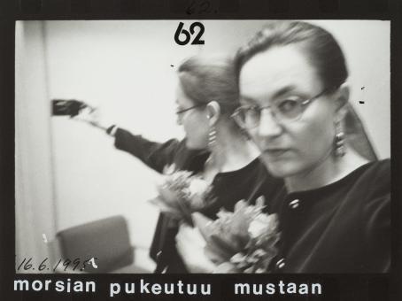 Heilahtaneessa mustavalkoisessa kuvassa nainen pitää kädessään kameraa ja hänen takanaan näkyy sama peilikuvana. Hänellä on kädessään kukkakimppu. Kuvan yläreunassa on numero 62 ja alareunassa päivämäärä 16.6.1995 sekä teksti "morsian pukeutuu mustaan".
