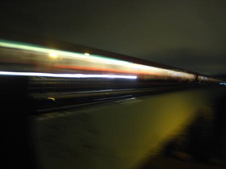 Valoviivoja jotka menevät kuvan poikki, muuten hämärää. Taaempana voi erottaa vähän junan ikkunoita.