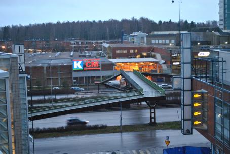 Ylhäältäpäin otetussa kuvassa näkyy autotie ja rakennuksia. Autotien yli menee kävelysilta. Isossa rakennuksessa on K-Citymarketin logo. Toisessa rakennuksessa lukee Itäkeskus ja Dinsko.