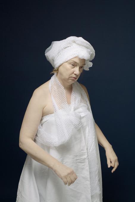 Nainen jolla on valkoisesta kankaasta tehty mekko, kaulassa huivi ja päässä samasta kankaasta kietaistu päähine. 