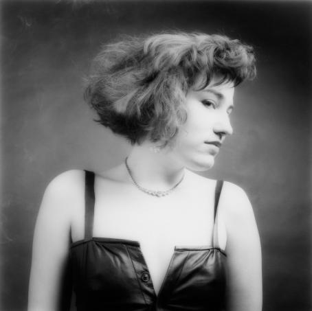 Tuija Lindström: Pia, 1983. Suomen valokuvataiteen museo / Finlands fotografiska museum / The Finnish Museum of Photography.<br /> Mustavalkoisessa kuvassa on nuori nainen mustassa nahkaisessa mekossa. Hänellä on lyhyt polkkatukka ja hän on kääntänyt päänsä sivulle.