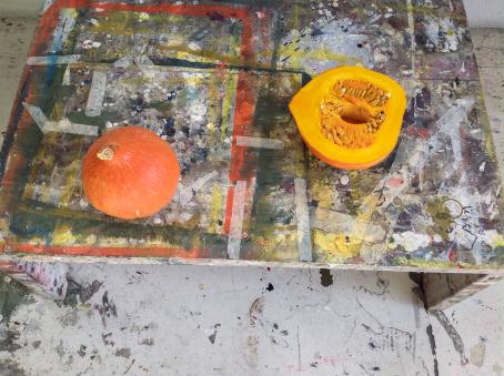 Tahraisen pöydän päällä on oranssi kokonainen kurpitsa, sekä puolikas kurpitsa.