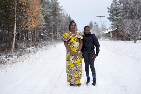 Kaksi tummaihoista naista seisoo keskellä lumista tietä. Toisella on keltainen mekko, toisella musta talvitakki ja mustat farkut.