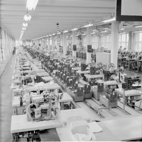 Näkymä isosta tehtaasta, missä työntekijät ompelevat ompelukoneilla.
