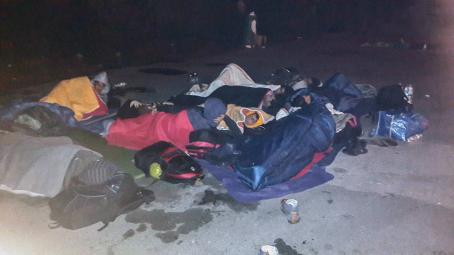 Pimeällä otettu kuva jossa ihmisiä nukkuu makuupusseissa maassa. Heidän ympärillään on reppuja ja laukkuja. 