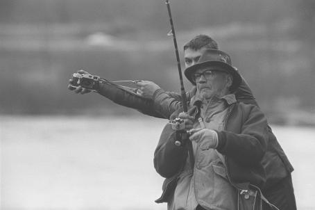 Presidentti epävirallisella vierailulla Ruotsissa, isäntänä ABU:n johtaja Georg Borgström. Kekkonen virvelöi kalaa Mörrum-joella valokuvaajan ahdistellessa. Kalle Kultala, Blekinge, Ruotsi, 1965. Suomen valokuvataiteen museo.