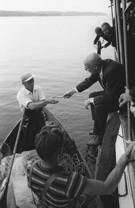 Urho Kekkonen keskustelee nuottaa näytösluonteisesti vetäneiden miesten kanssa ja tarjoaa heille sikarit. Kalle Kultala, Savonlinna, 1961. Suomen valokuvataiteen museo.