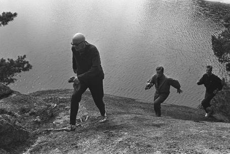 Presidentti Urho Kekkonen osallistuu Paavon polku -kuntotapahtumaan. Kekkonen nousee ylös rantakalliota, perässä puolustusministeri kenraalimajuri Kaarlo Leinonen. Kalle Kultala, Upinniemi, 1964. Suomen valokuvataiteen museo.