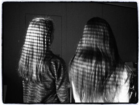 Mustavalkoisessa kuvassa kaksi pitkähiuksista henkilöä selin kameraan. Aurinko paistaa ilmeisesti sälekaihtimien raoista, tehden henkilöiden hiuksiin valoraitoja. 