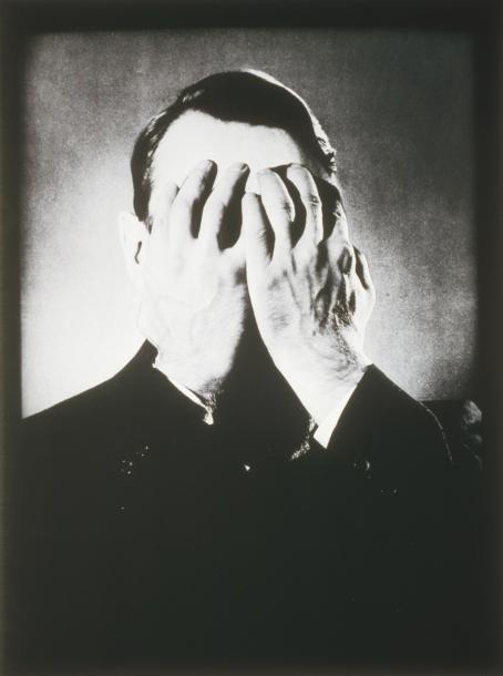 Mustavalkoisessa kuvassa Mauno Koivisto. Hänellä on kädet kasvojensa edessä. 