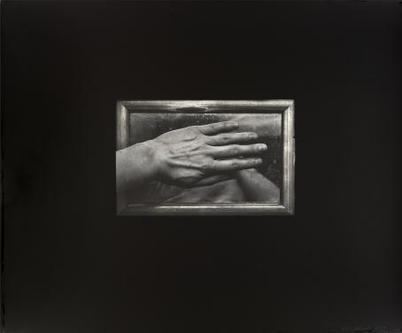 Mustan alueen keskellä on mustavalkoinen kuva, jossa on kehyksissä oleva peili, joka on peitetty kädellä. Käsi peittää lähes koko alueen, mutta peilistä voi erottaa ihmisen käsivartta ja muita muotoja. 