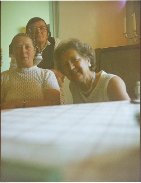 Kolme vanhempaa naista istuu pöydän ääressä. Kuva on otettu pöydän tasolta niin että pöytä peittää lähes puolet kuvasta alhaalta. 