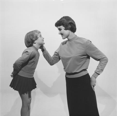 Mustavalkoisessa kuvassa nainen ja lapsi katsovat toisiaan. Nainen pitää kättään lapsen poskella. Lapsi on naisen kanssa lähes samalla tasolla. Molemmilla on päällään yksinkertaiset pitkähihaiset paidat ja tummat hameet. Lapsen hame on todella lyhyt, naisen taas pitkä. 