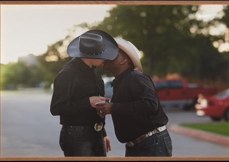 Kaksi cowboytä suutelee International Gay Rodeo -tapahtuman finaaleissa Fort Worthissa, Yhdysvalloissa. Stetsonit peittävät puolikuvassa kuvattujen henkilöiden kasvonsa. Heillä on käsissään kertakäyttöiset kahvimukit.